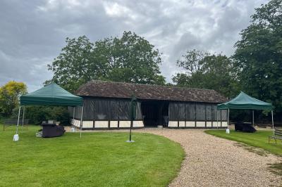 Salle de réception rustique avec poutres en bois apparentes, tables rondes dressées et chaises rouges.