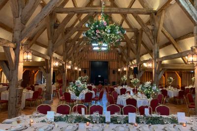 Salle de réception rustique avec poutres en bois apparentes, tables rondes dressées et chaises rouges.