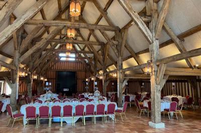 Salle de réception rustique avec poutres en bois apparentes, tables rondes dressées et chaises rouges.