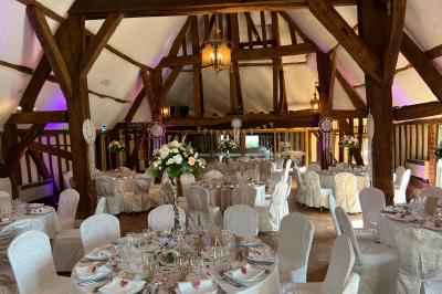 Salle de réception rustique avec poutres en bois apparentes, tables rondes dressées et chaises rouges.