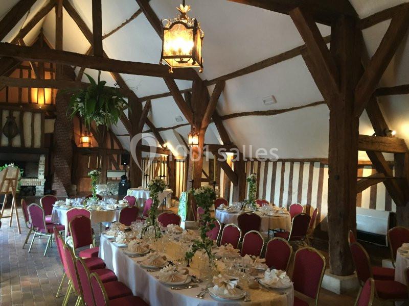 Salle de réception rustique avec poutres apparentes, tables rondes dressées et chaises rouges, décorée pour un événement.