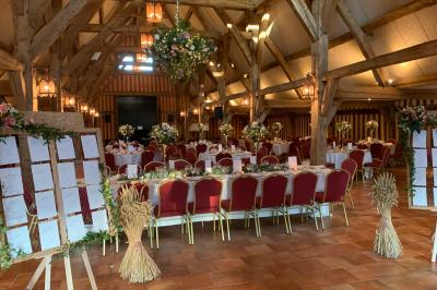 Salle de réception rustique avec poutres en bois apparentes, tables rondes dressées et chaises rouges.