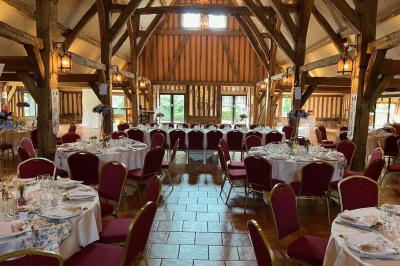 Salle de réception rustique avec poutres en bois apparentes, tables rondes dressées et chaises rouges.