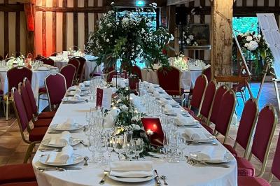 Salle de réception rustique avec poutres en bois apparentes, tables rondes dressées et chaises rouges.