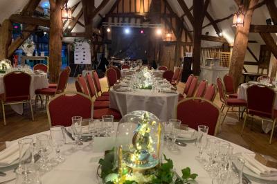 Salle de réception rustique avec poutres en bois apparentes, tables rondes dressées et chaises rouges.