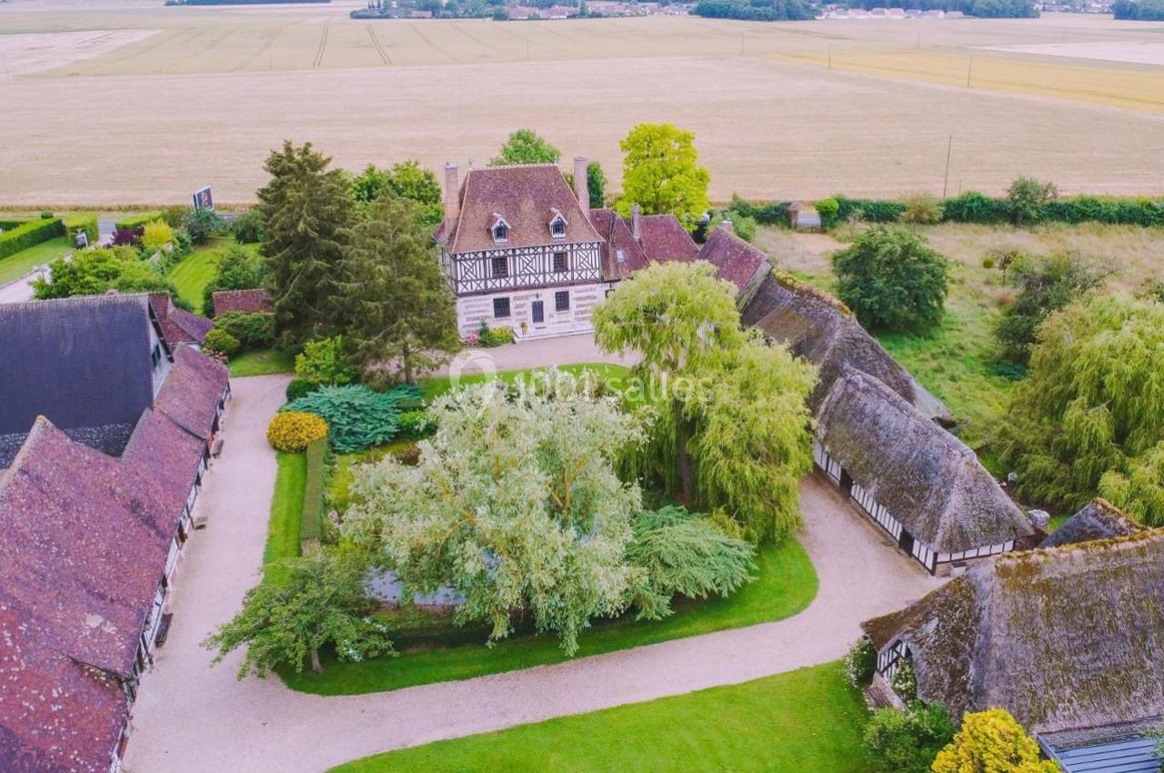 Vue aérienne d'une ferme traditionnelle avec bâtiments à colombages entourés de jardins et de champs.