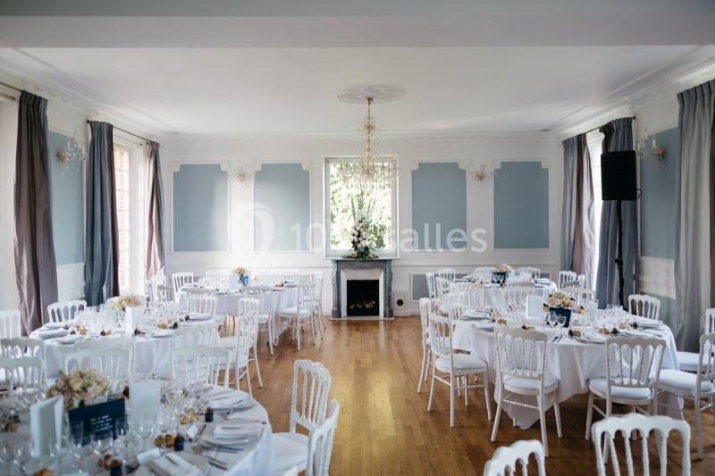 Salle de réception lumineuse avec tables rondes dressées, chaises blanches et décoration élégante.