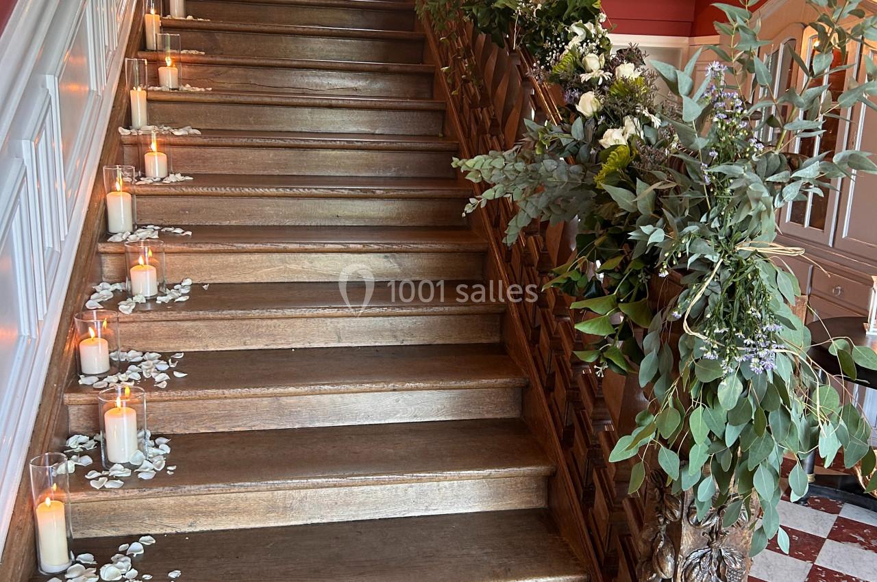 Escalier en bois décoré de bougies, pétales de fleurs blanches et guirlandes de feuillage, dans un intérieur lumineux.