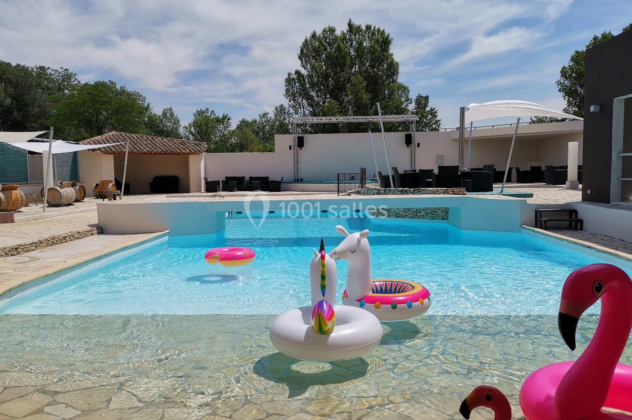 Piscine extérieure avec des bouées colorées en forme d'animaux, entourée de chaises et d'arbres sous un ciel dégagé.