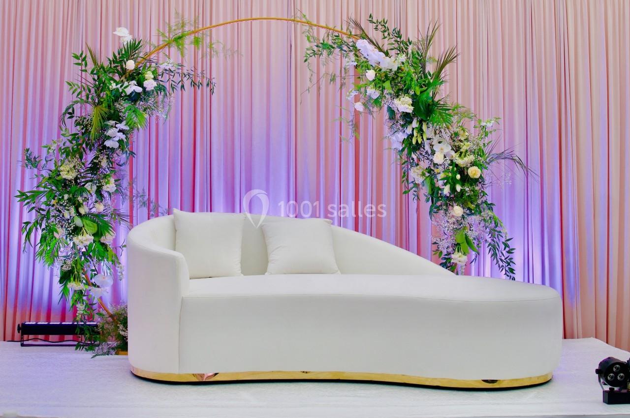 Canapé blanc incurvé devant un fond de rideaux roses, décoré d'arcs floraux avec des fleurs blanches et vertes.