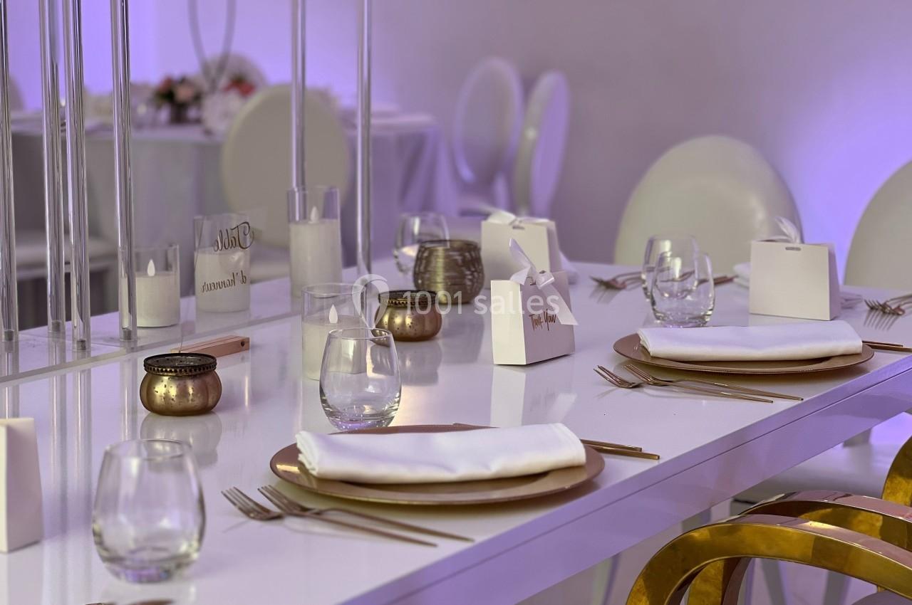 Table élégamment dressée avec assiettes dorées, serviettes blanches, verres et décorations minimalistes dans un cadre…