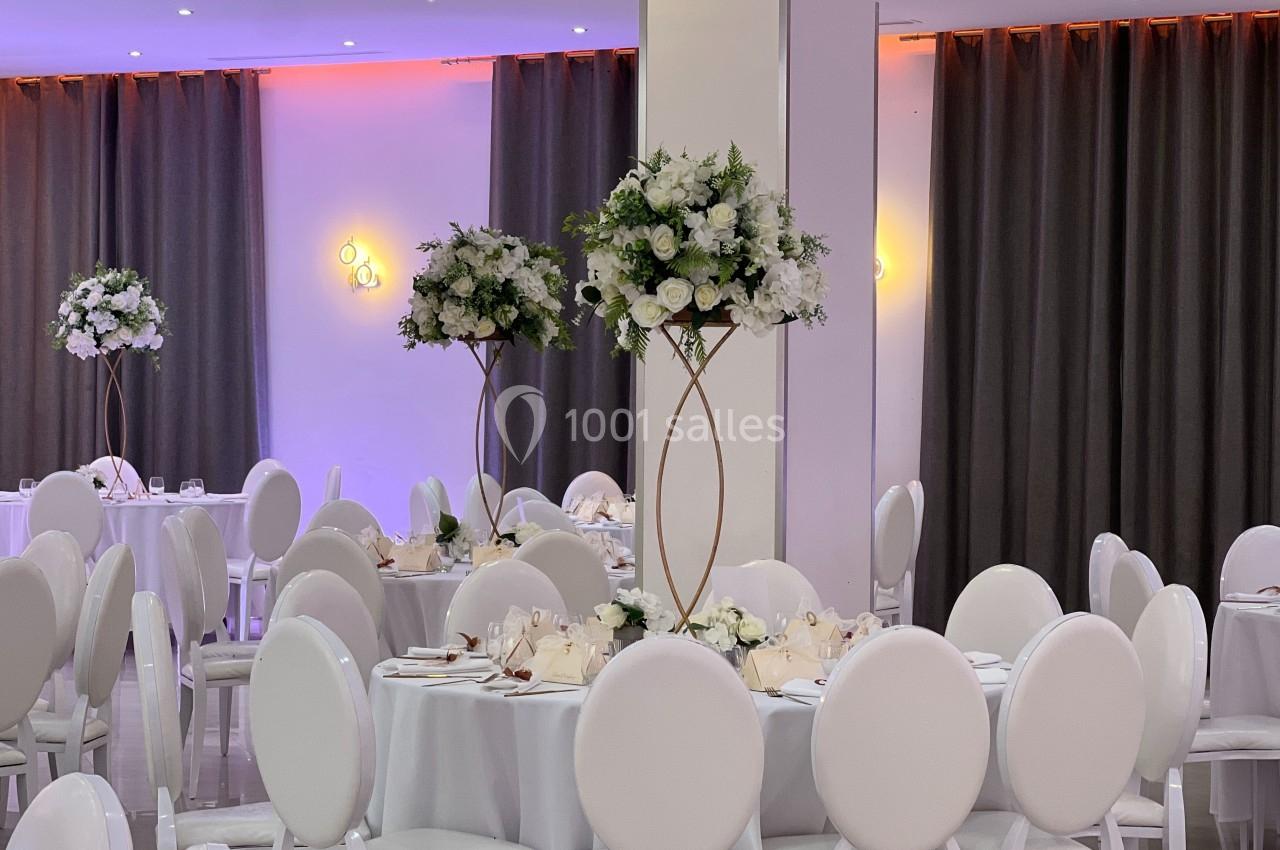 Salle de réception élégante avec des tables décorées de nappes blanches et des centres de table fleuris.