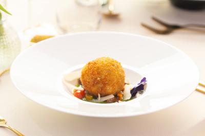 Rouleau croustillant servi sur un lit de légumes colorés avec une garniture florale sur une assiette blanche.
