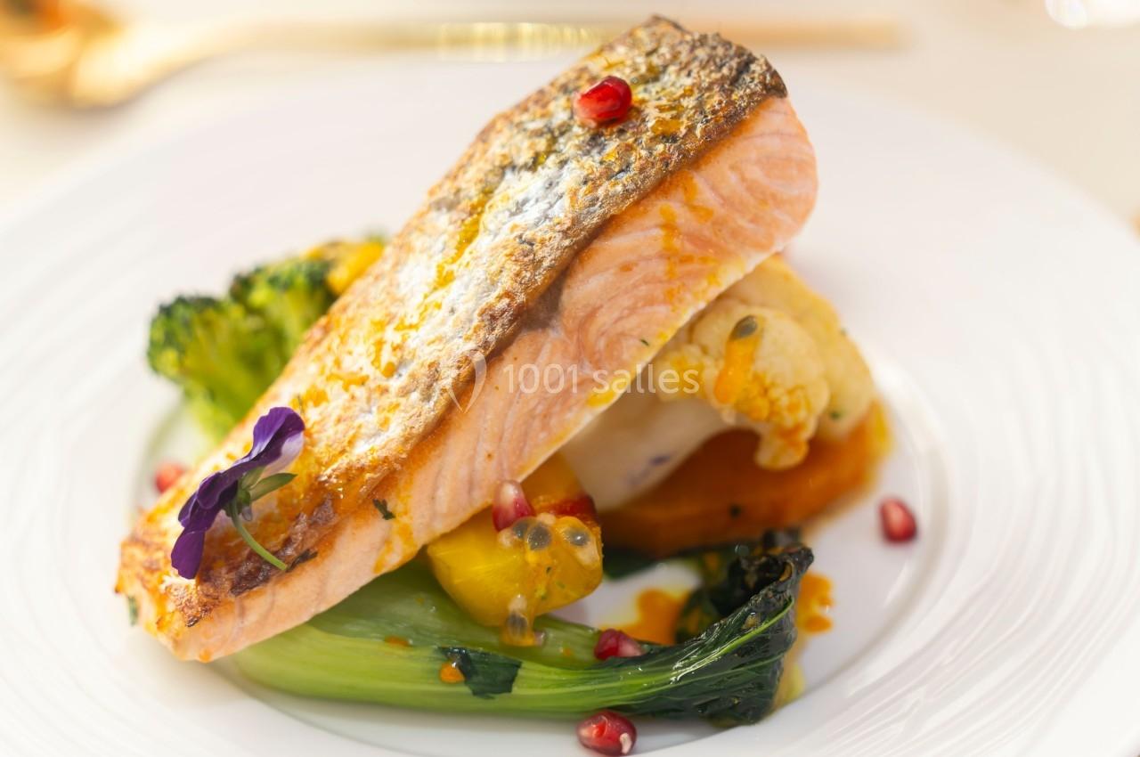 Filet de saumon grillé servi avec légumes variés, purée et graines de grenade sur une assiette blanche.