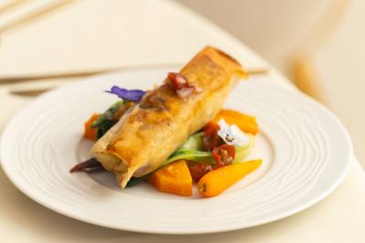 Rouleau croustillant servi sur un lit de légumes colorés avec une garniture florale sur une assiette blanche.