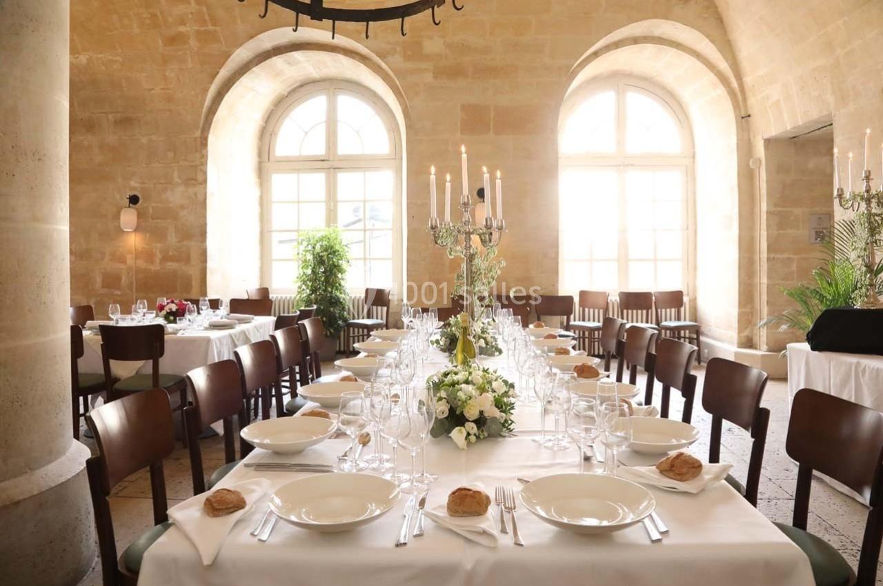 Location salle Chantilly (Oise) - La Capitainerie du Château de Chantilly #2 Salle de réception lumineuse avec une grande table dressée, ornée de fleurs et de chandeliers, entourée de chaises.
