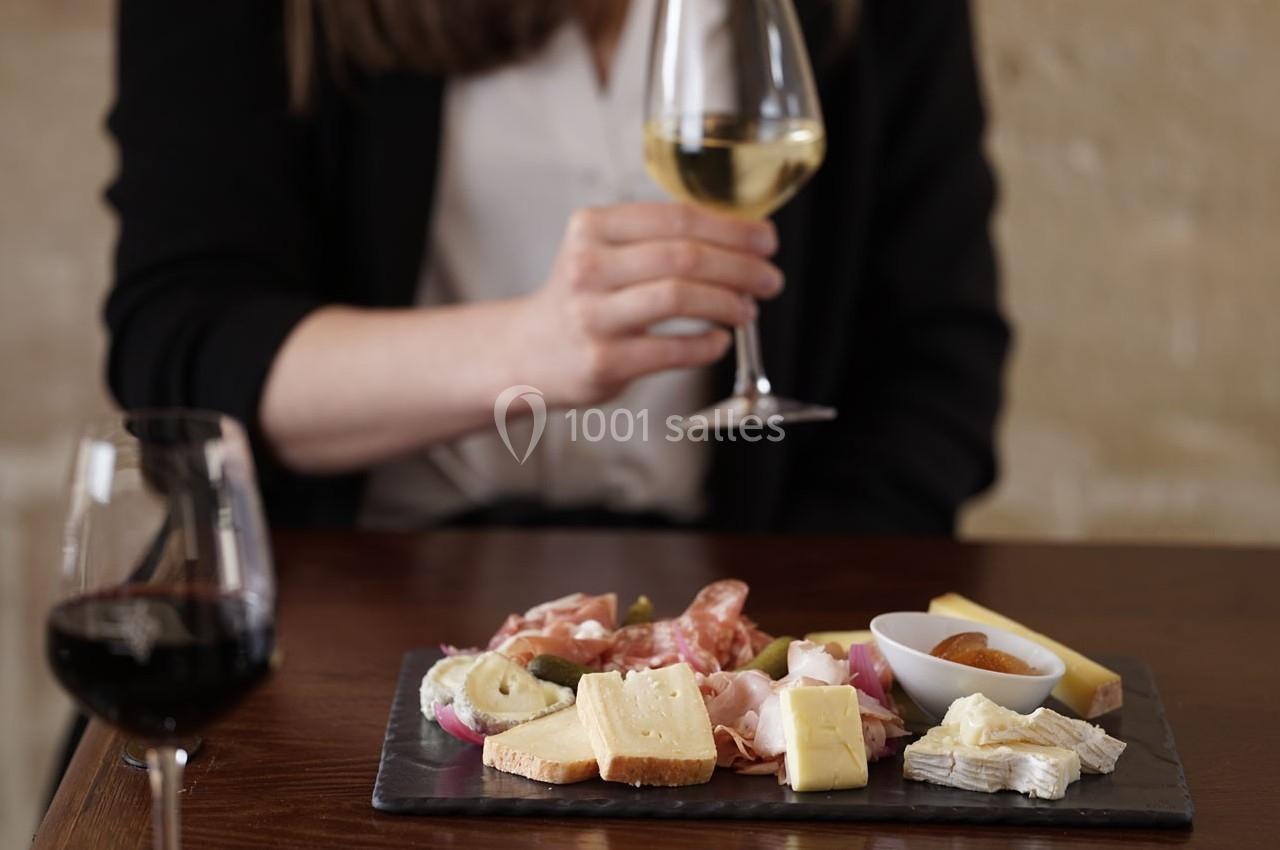 Location salle Chantilly (Oise) - La Capitainerie du Château de Chantilly #5 Plateau de fromages et charcuteries sur une table, avec une personne tenant un verre de vin blanc.