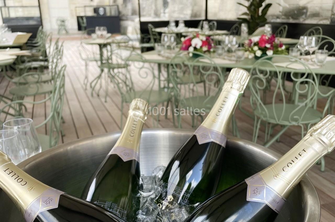 Location salle Chantilly (Oise) - La Capitainerie du Château de Chantilly #10 Bouteilles de champagne dans un seau à glace sur une terrasse avec tables et chaises en métal vert clair.