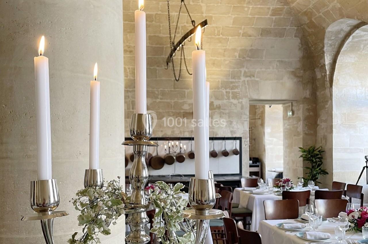 Location salle Chantilly (Oise) - La Capitainerie du Château de Chantilly #14 Chandelier argenté avec bougies allumées, décoré de feuillage, dans une salle de réception en pierre avec tables dressées.