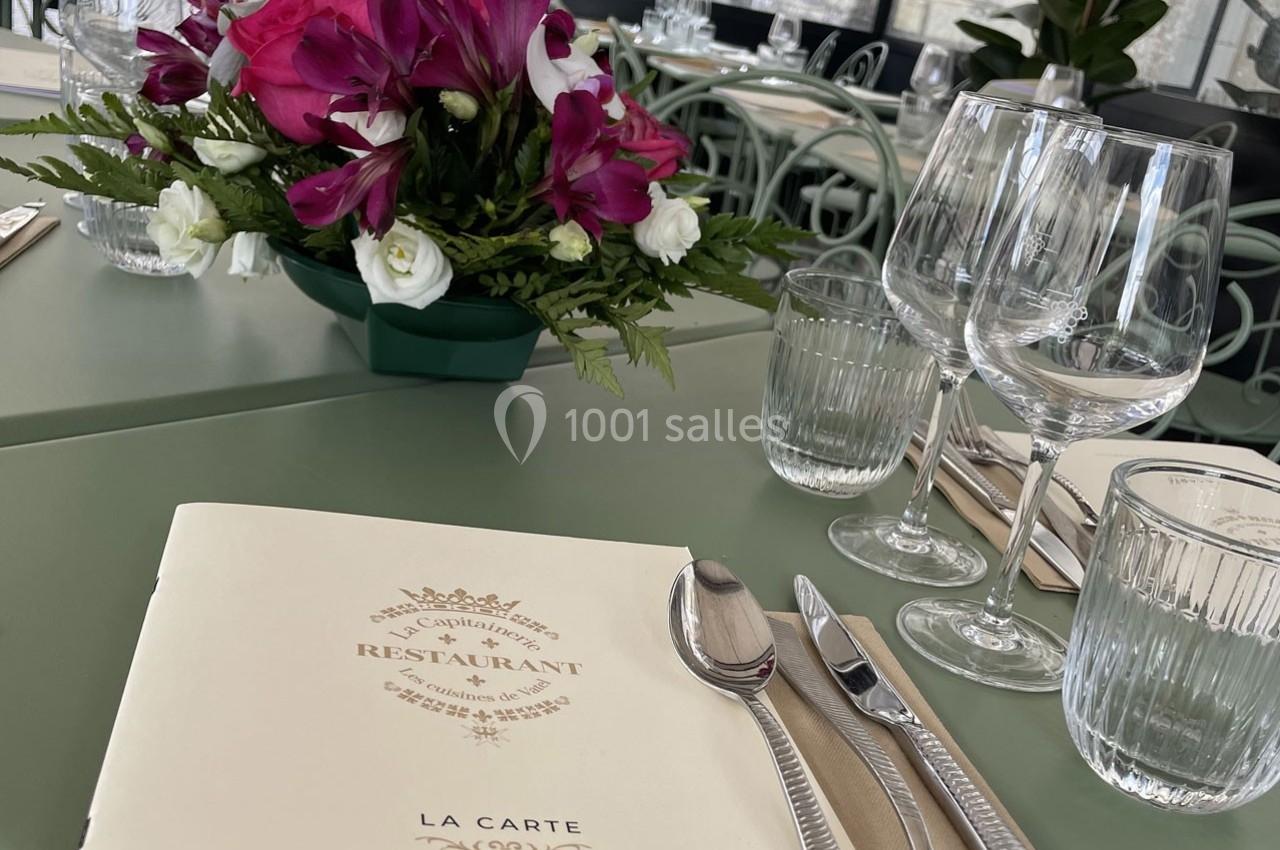 Location salle Chantilly (Oise) - La Capitainerie du Château de Chantilly #20 Menu posé sur une table dressée avec des couverts, verres et un bouquet de fleurs en arrière-plan.