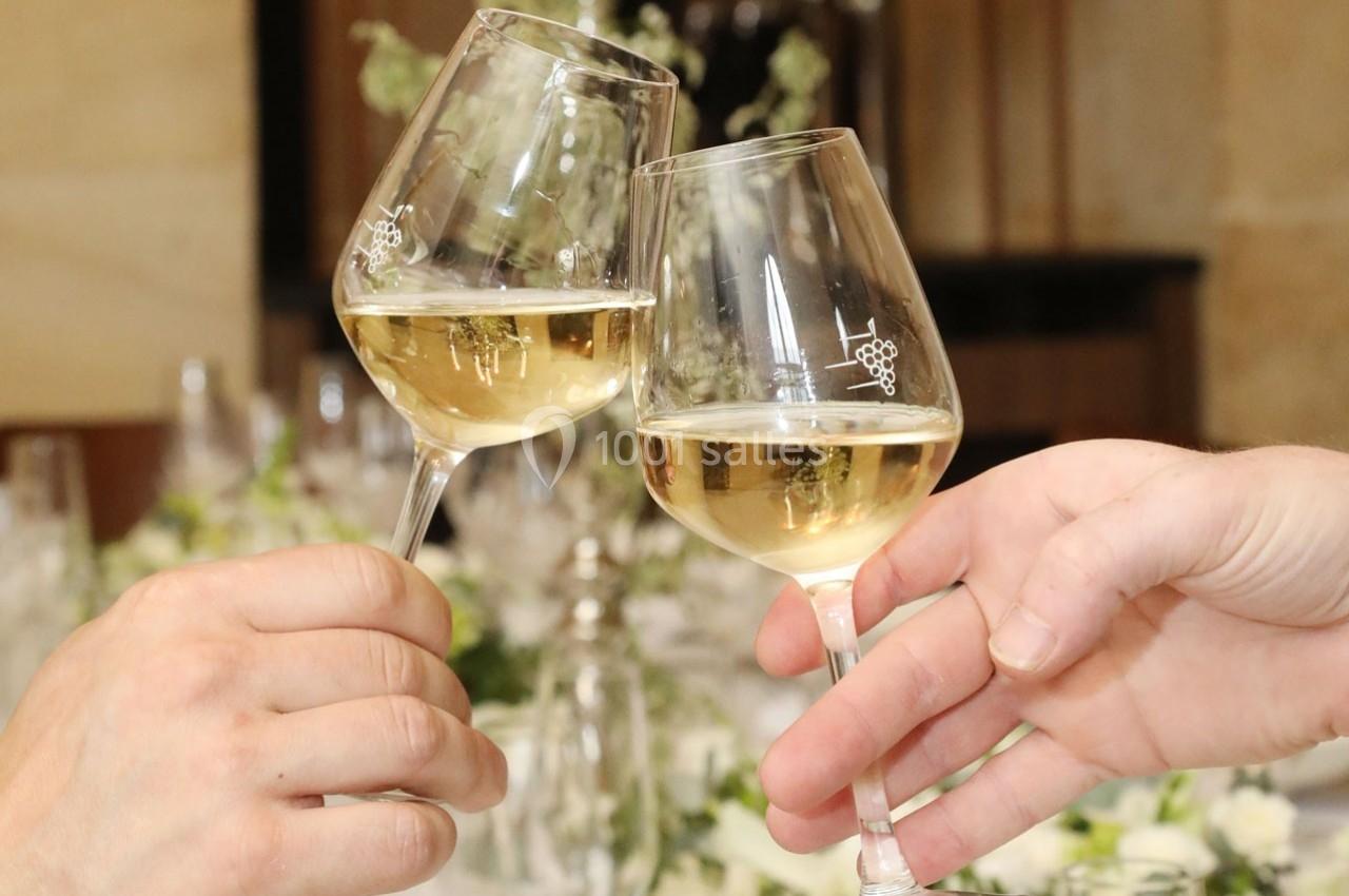 Location salle Chantilly (Oise) - La Capitainerie du Château de Chantilly #22 Deux verres de vin blanc portés pour un toast, avec une table décorée en arrière-plan flou.