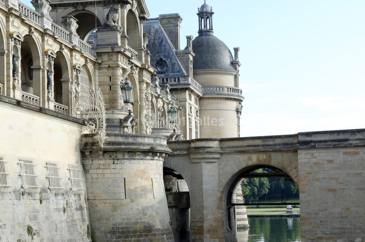 Location salle Chantilly (Oise) - La Capitainerie du Château de Chantilly #25 Façade d'un château en pierre avec arcades, tourelles et pont au-dessus d'un plan d'eau calme.