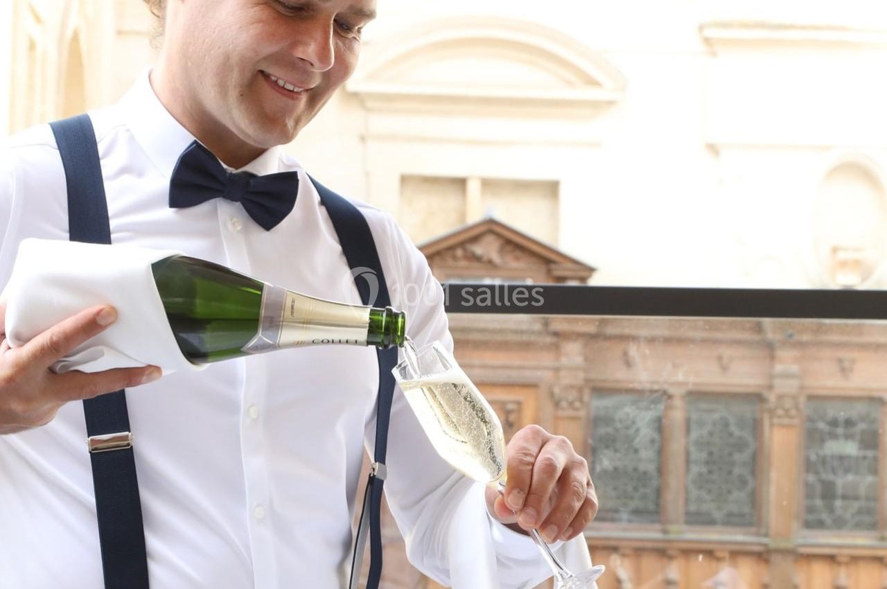 Location salle Chantilly (Oise) - La Capitainerie du Château de Chantilly #26 Un serveur en tenue élégante verse du champagne dans une flûte sur une terrasse avec un bâtiment en arrière-plan.