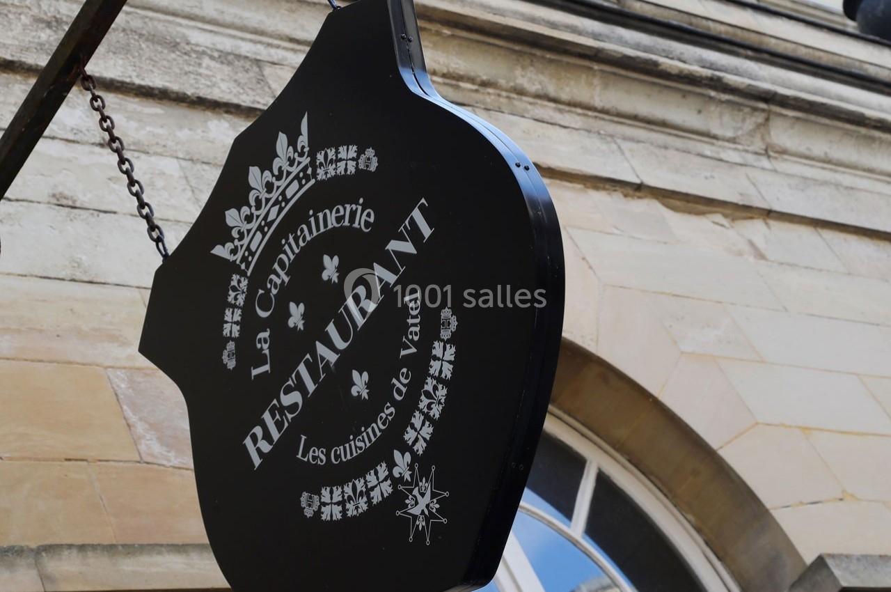Location salle Chantilly (Oise) - La Capitainerie du Château de Chantilly #29 Enseigne noire suspendue indiquant ’La Capitainerie Restaurant, Les cuisines de Vatel’ devant un bâtiment en pierre.