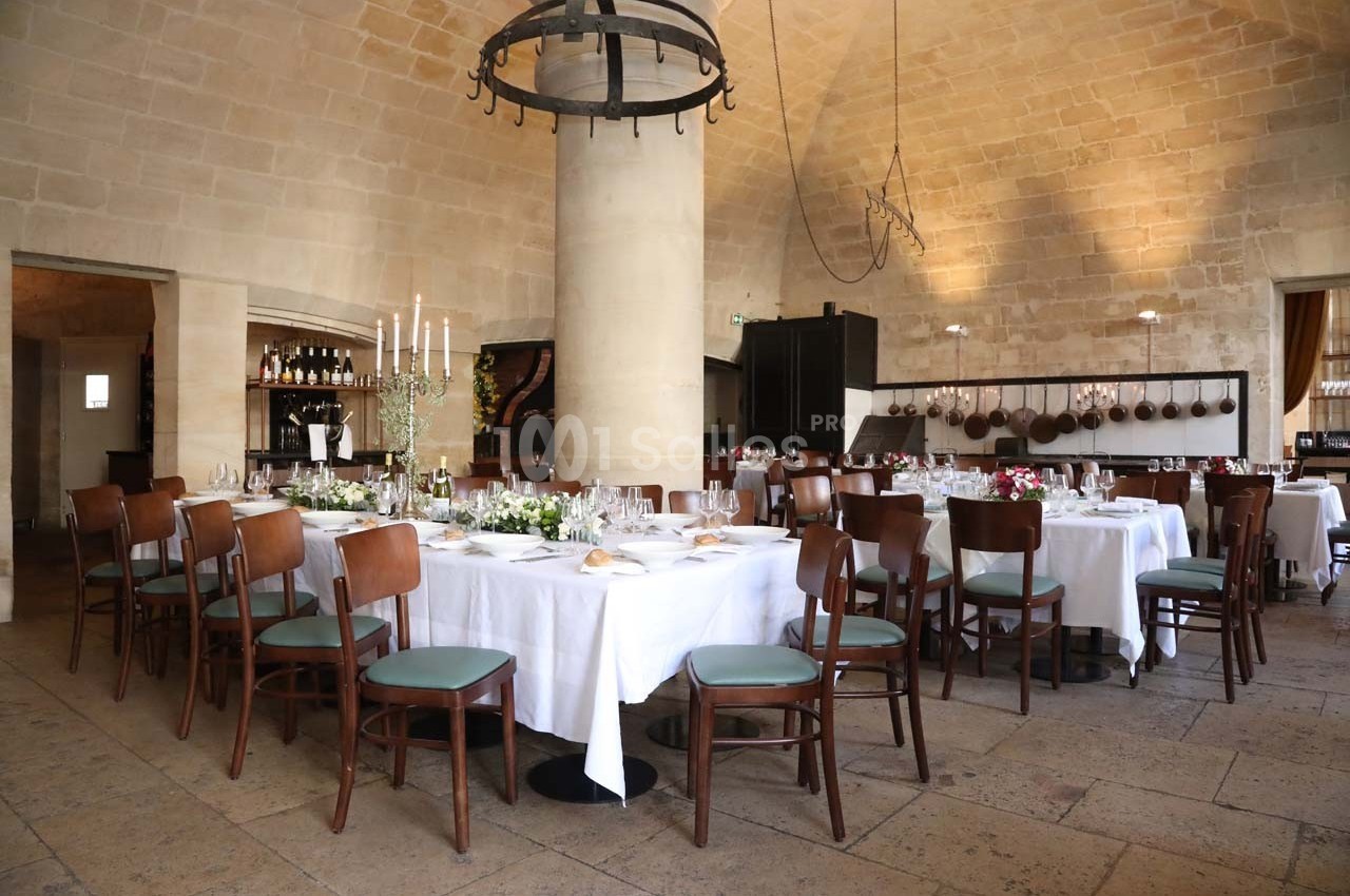 Salle de restaurant élégante avec tables dressées, nappes blanches, chaises en bois et décor en pierre voûtée.