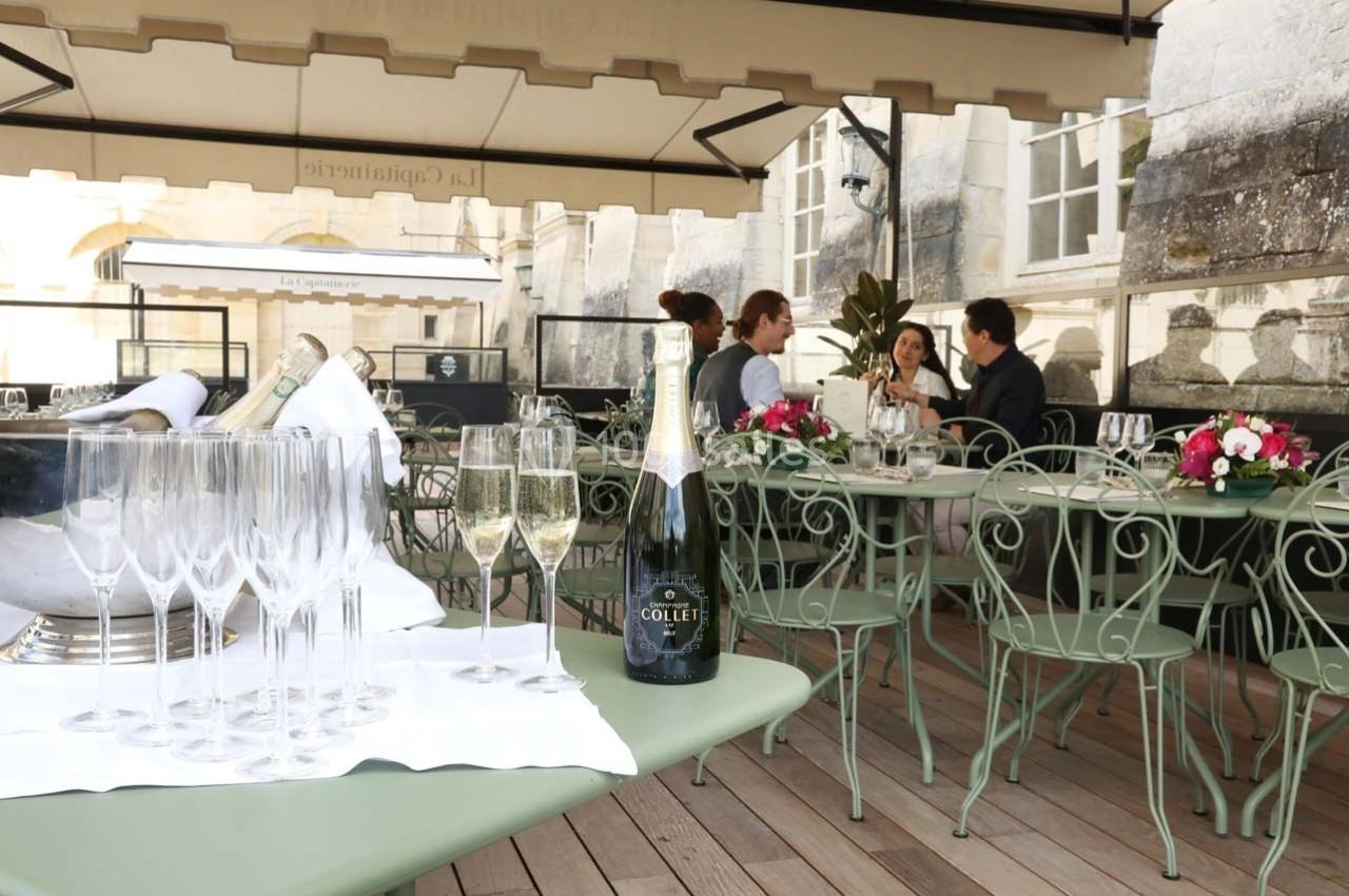 Terrasse avec tables en fer forgé, flûtes de champagne et un groupe de personnes en discussion au fond.