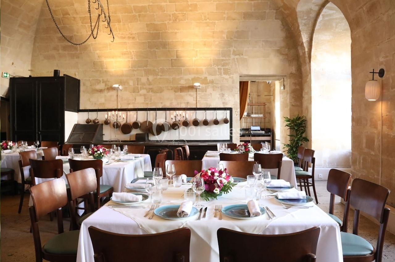 Salle de restaurant lumineuse avec tables dressées, nappes blanches, chaises en bois et décoration florale.