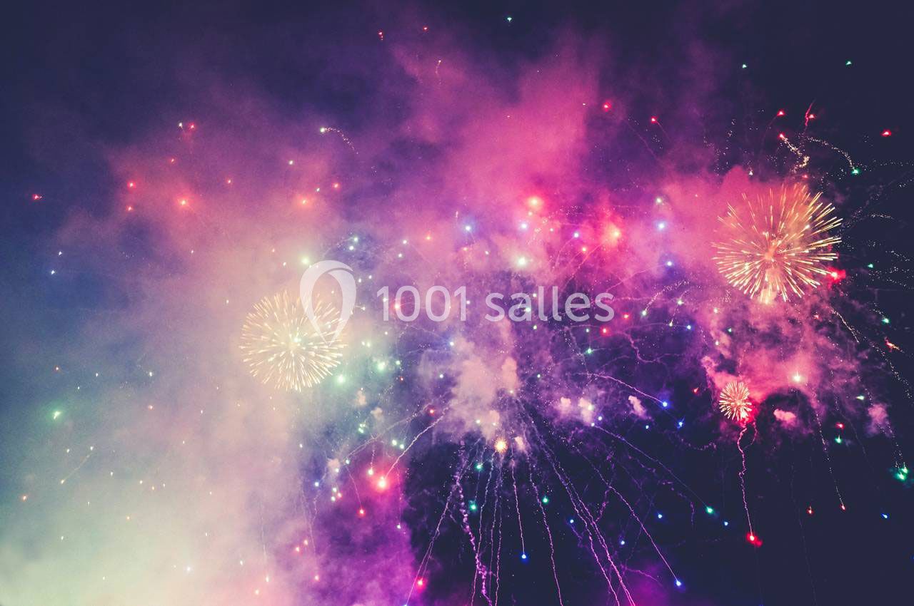 Feux d'artifice multicolores illuminant un ciel nocturne avec des éclats de lumière et de fumée.