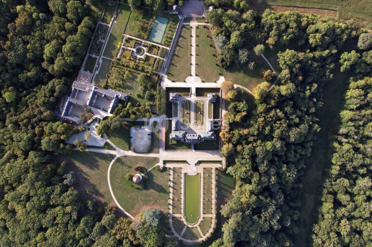 Vue aérienne d'un château entouré de jardins symétriques, bassins et forêt dense.