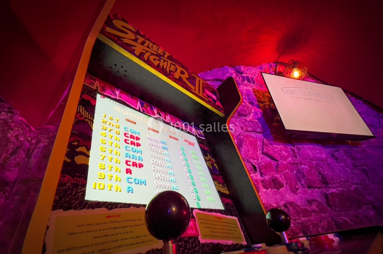 Borne d'arcade rétro allumée affichant un classement de scores, avec un mur en briques en arrière-plan.