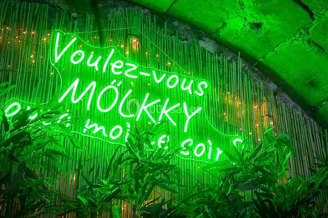 Enseigne néon verte ’Voulez-vous mölkky avec moi ce soir ?’ sur fond de bambou et feuillage.