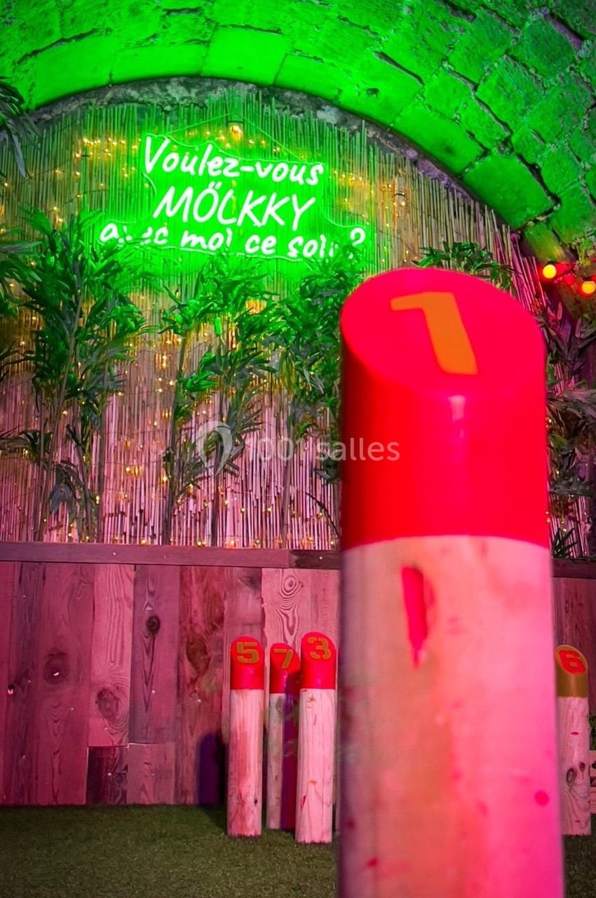 Quilles de mölkky numérotées sur un terrain en gazon artificiel, sous un éclairage coloré et un néon vert.