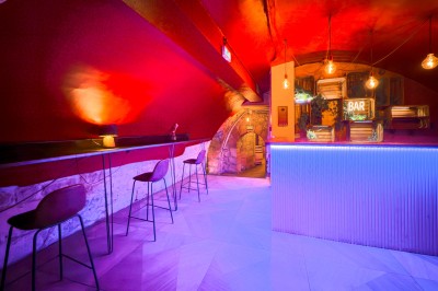 Comptoir lumineux dans une pièce voûtée en pierre, décoré de plantes, lampes et guirlandes lumineuses.