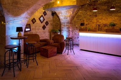 Comptoir lumineux dans une pièce voûtée en pierre, décoré de plantes, lampes et guirlandes lumineuses.