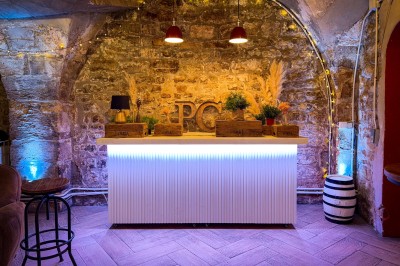 Comptoir lumineux dans une pièce voûtée en pierre, décoré de plantes, lampes et guirlandes lumineuses.