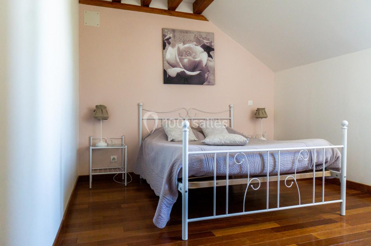 Chambre avec lit double en métal blanc, parquet en bois, murs clairs et tableau floral au-dessus du lit.