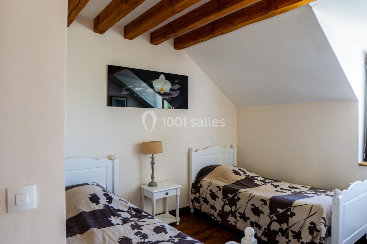 Deux lits simples avec couvre-lits à motifs floraux dans une chambre lumineuse avec poutres apparentes en bois.