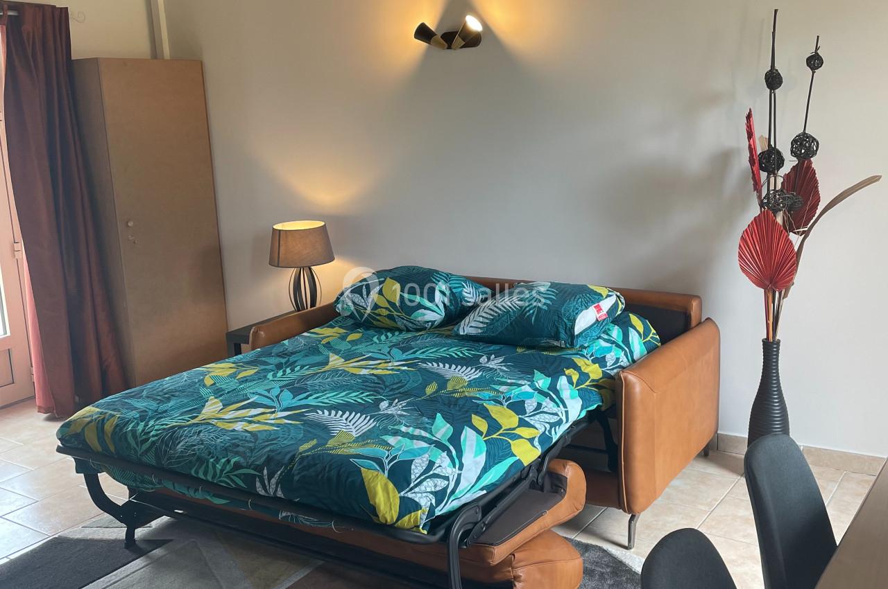 Canapé-lit déplié avec une housse à motifs tropicaux, dans un salon lumineux avec poutres apparentes et décoration moderne.