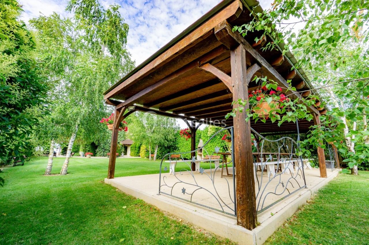 Pergola en bois dans un jardin verdoyant, ornée de fleurs suspendues et entourée d'arbres et de pelouse.