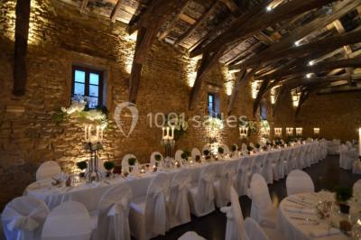 Cour éclairée au crépuscule avec des bâtiments en pierre, des torches allumées et des personnes en arrière-plan.