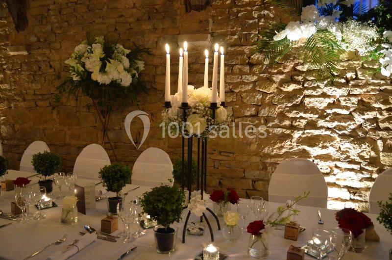 Table décorée pour un dîner élégant avec chandeliers, fleurs blanches et rouges, et murs en pierre en arrière-plan.