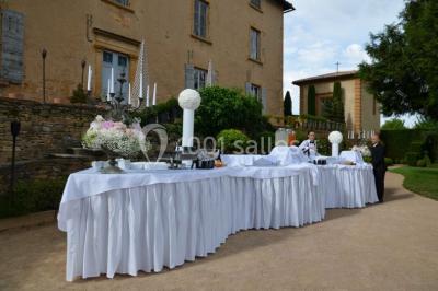 Cour éclairée au crépuscule avec des bâtiments en pierre, des torches allumées et des personnes en arrière-plan.