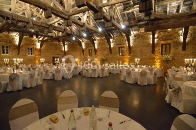 Cour éclairée au crépuscule avec des bâtiments en pierre, des torches allumées et des personnes en arrière-plan.