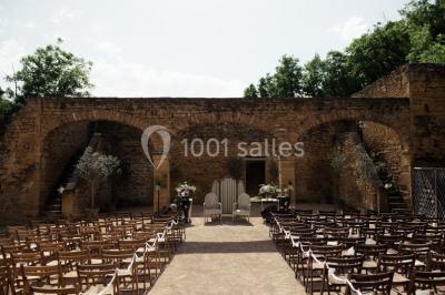 Cour éclairée au crépuscule avec des bâtiments en pierre, des torches allumées et des personnes en arrière-plan.