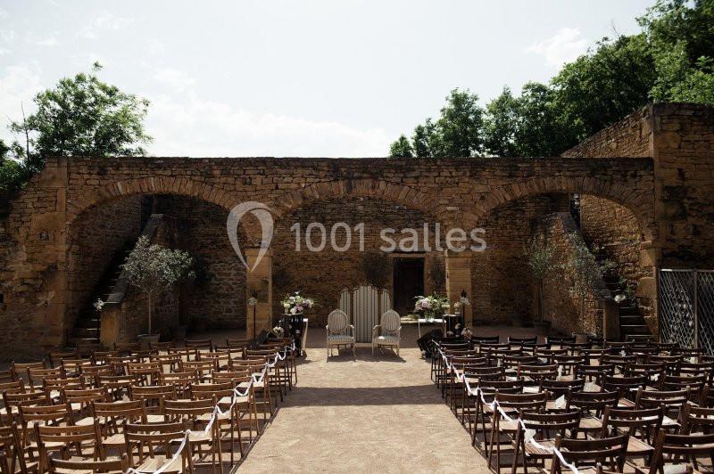 Disposition de chaises en plein air face à une arche en pierre, préparée pour une cérémonie dans une cour historique.