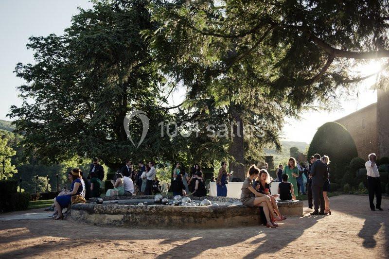 Des personnes discutent autour d'une fontaine dans un jardin ombragé, entouré d'arbres et de verdure.